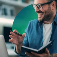 Man with glasses smiling with notebook and laptop